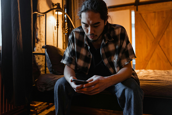 Man on bed looking at phone, appearing upset, in a dimly lit room. Man on bed looking at phone, appearing upset, in a dimly lit room.