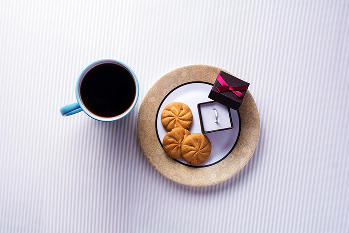 A ring in a box next to cookies and coffee symbolizes marriage discussions. A ring in a box next to cookies and coffee symbolizes marriage discussions.