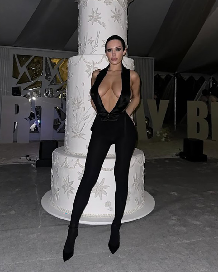 Person in a revealing black outfit standing in front of a large ornate cake. Person in a revealing black outfit standing in front of a large ornate cake.