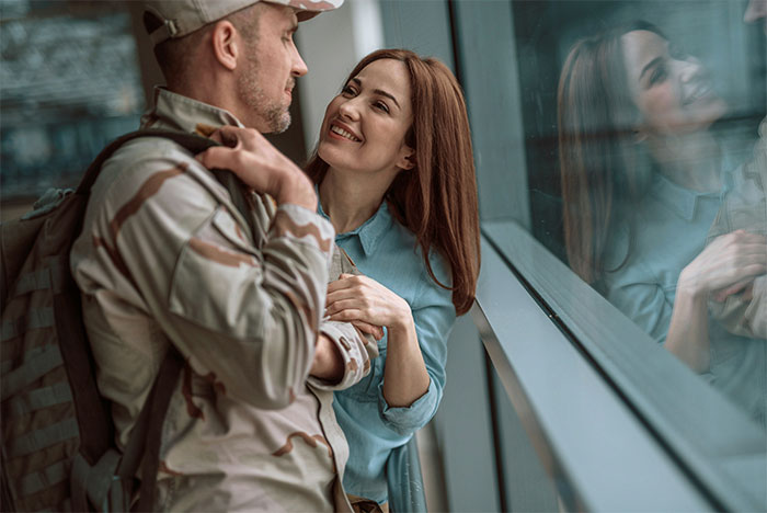 Man in military uniform embraces smiling woman by a window, illustrating marriage themes. Man in military uniform embraces smiling woman by a window, illustrating marriage themes.