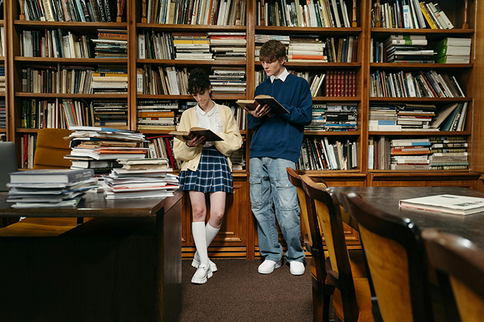 Two students reading in a library, surrounded by bookshelves and stacks of books. Two students reading in a library, surrounded by bookshelves and stacks of books.