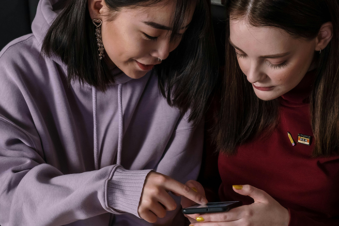 Two women looking at a phone together, engaged in conversation about a vacation ban. Two women looking at a phone together, engaged in conversation about a vacation ban.