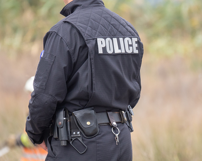 Police officer in uniform outdoors, with "POLICE" visible on the back. Police officer in uniform outdoors, with "POLICE" visible on the back.