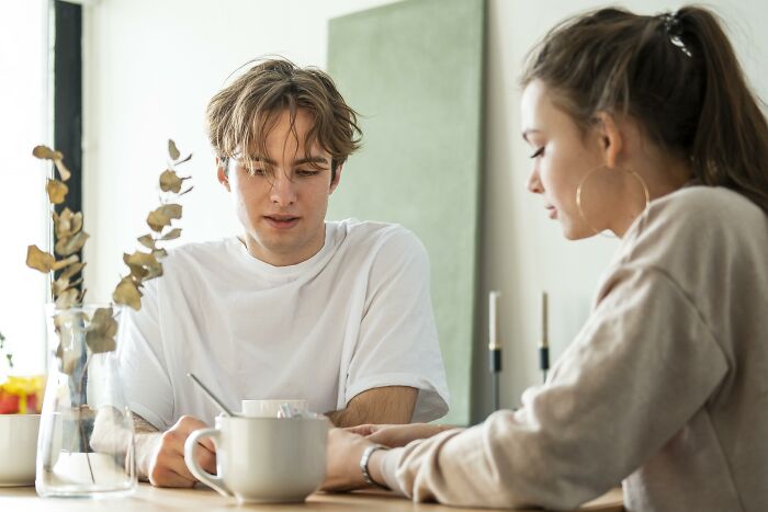 Young couple having a serious conversation at a table, showing tension related to paying and jealousy issues in their relationship. Young couple having a serious conversation at a table, showing tension related to paying and jealousy issues in their relationship.