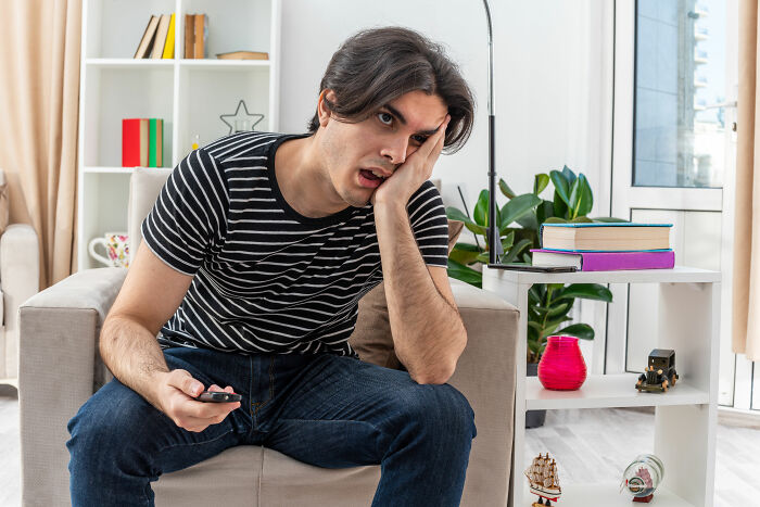 Young man in striped shirt looking frustrated while sitting on couch, reflecting tension in a relationship involving financial disputes. Young man in striped shirt looking frustrated while sitting on couch, reflecting tension in a relationship involving financial disputes.