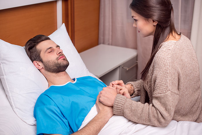 Man in ER bed while girlfriend holds his hand, phone nearby, tension in the air. Man in ER bed while girlfriend holds his hand, phone nearby, tension in the air.