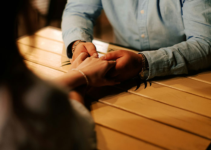 A couple holding hands across a table in a dimly lit setting, suggesting a reconciliation or deep conversation. A couple holding hands across a table in a dimly lit setting, suggesting a reconciliation or deep conversation.
