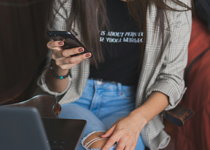 A woman in a plaid jacket, using her phone while sitting in front of a laptop, representing relationship challenges. A woman in a plaid jacket, using her phone while sitting in front of a laptop, representing relationship challenges.