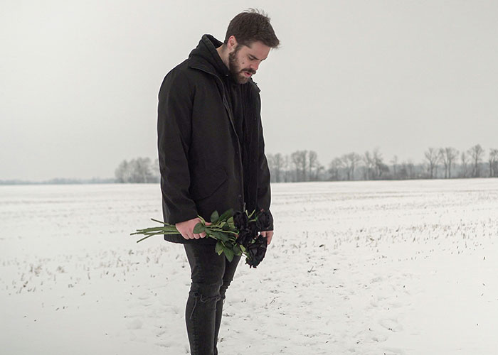 Man in black coat standing in snowy field, holding wilted flowers, symbolizing lost love after breakup. Man in black coat standing in snowy field, holding wilted flowers, symbolizing lost love after breakup.