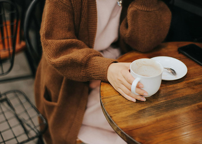 Woman in a cozy cafe, wearing a brown sweater, holding a coffee mug, relating to breakup and reconciliation themes. Woman in a cozy cafe, wearing a brown sweater, holding a coffee mug, relating to breakup and reconciliation themes.