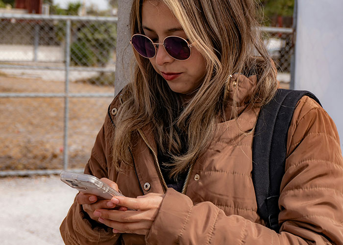 Woman wearing sunglasses using her phone outdoors, bundled in a brown jacket. Woman wearing sunglasses using her phone outdoors, bundled in a brown jacket.