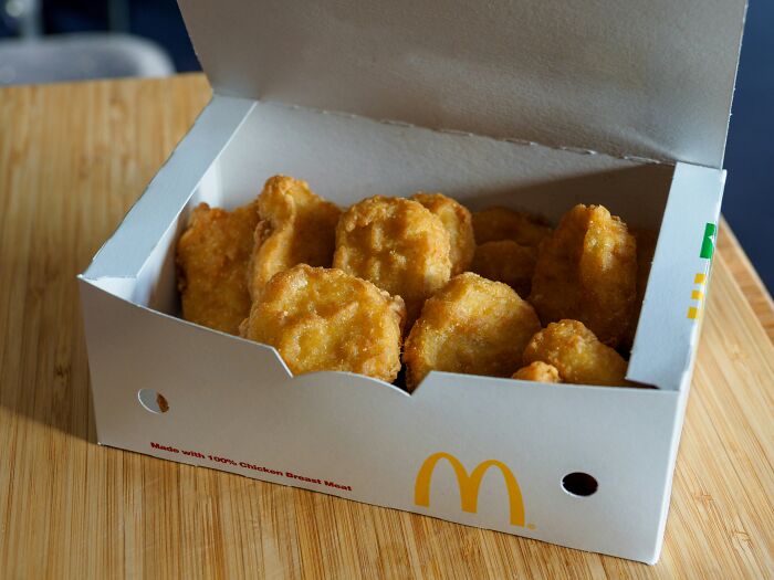 Box of McDonald's chicken nuggets on a wooden table, open with several pieces inside, showcasing fast food delight.