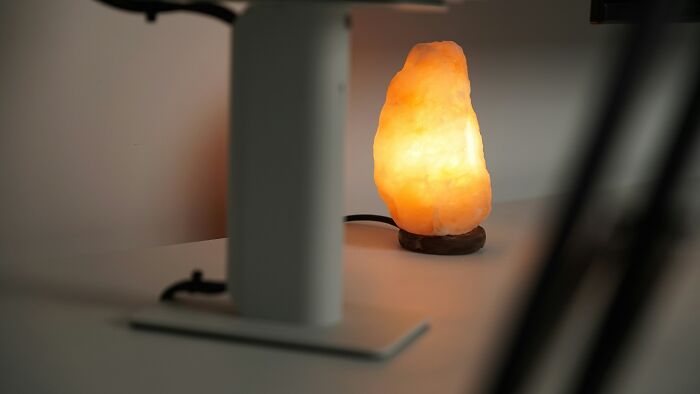 A glowing Himalayan salt lamp on a desk near a metal stand, creating a warm ambiance.