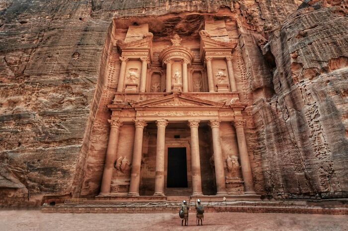 Ancient man-made structure carved into sandstone cliffs with columns and intricate architectural details.