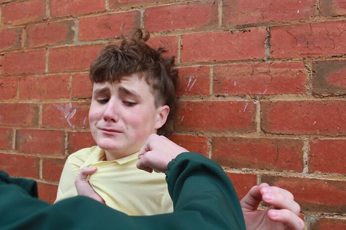 A person in distress against a brick wall during a confrontation, highlighting bullying dynamics.