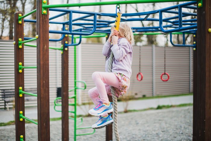 Child climbing a rope on a colorful swing set at playground, highlighting woman buying swing set for her kid. Child climbing a rope on a colorful swing set at playground, highlighting woman buying swing set for her kid.