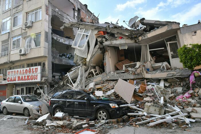 Collapsed building debris on street with damaged cars, illustrating a super normal thing in a country prone to natural disasters.