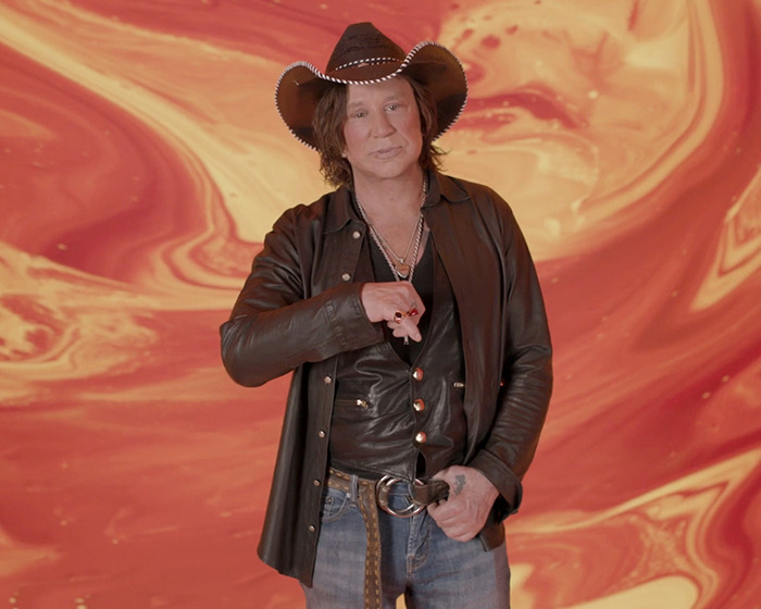 Cowboy hat-wearing individual in leather jacket, with abstract orange background, relating to Celebrity Big Brother controversy. Cowboy hat-wearing individual in leather jacket, with abstract orange background, relating to Celebrity Big Brother controversy.