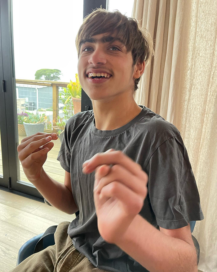 Young person in a gray shirt smiling indoors with natural light, related to Colin Farrell's family. Young person in a gray shirt smiling indoors with natural light, related to Colin Farrell's family.