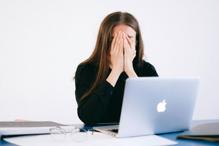 Woman holds face in frustration during a video call, feeling devastated by coworkers' remarks. Woman holds face in frustration during a video call, feeling devastated by coworkers' remarks.