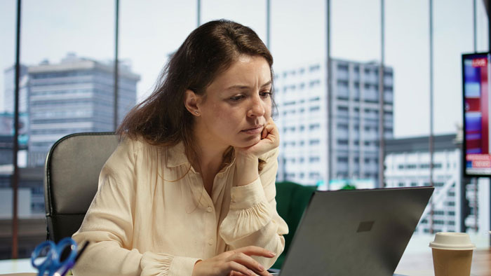 Woman on video call, looking concerned, overhearing coworkers' comments in an office setting. Woman on video call, looking concerned, overhearing coworkers' comments in an office setting.