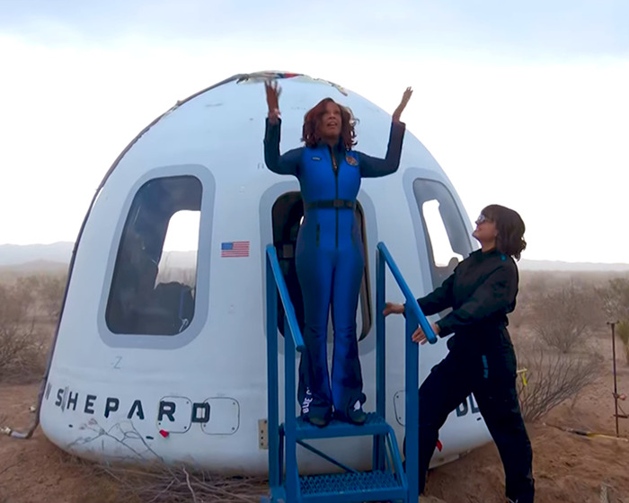 Person in blue suit atop stairs near Blue Origin capsule as another looks, with a desert backdrop. Person in blue suit atop stairs near Blue Origin capsule as another looks, with a desert backdrop.