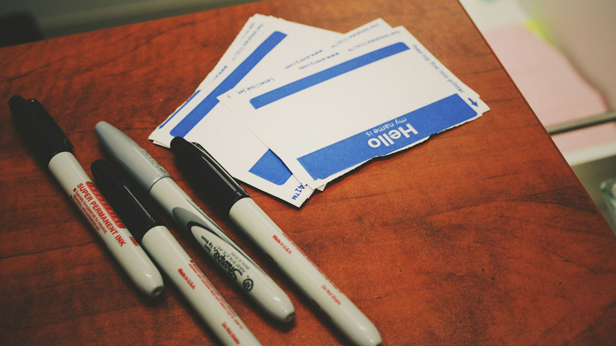 Several markers and blank name tags on a wooden table, ready for writing cool last names.