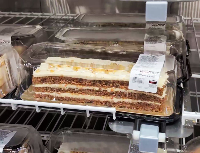Costco carrot cake slice in plastic container on store shelf, featuring layers and white frosting. Costco carrot cake slice in plastic container on store shelf, featuring layers and white frosting.