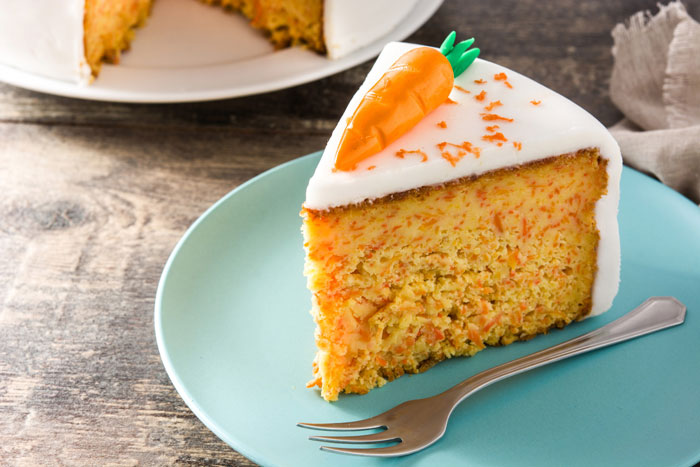 Slice of carrot cake on a blue plate with icing and garnished with a fondant carrot, sparking debate among Costco shoppers. Slice of carrot cake on a blue plate with icing and garnished with a fondant carrot, sparking debate among Costco shoppers.