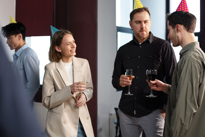 Coworkers in party hats discuss a gluten-free diet while holding drinks, illustrating personal sharing at work events. Coworkers in party hats discuss a gluten-free diet while holding drinks, illustrating personal sharing at work events.