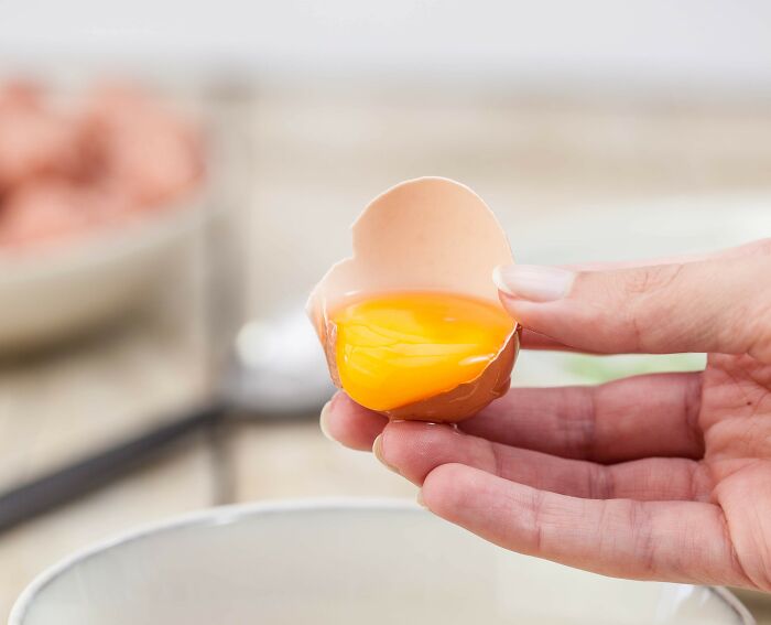 Hand holding a c*****d egg with yolk, showcasing an American kitchen habit that might seem unusual to non-Americans.