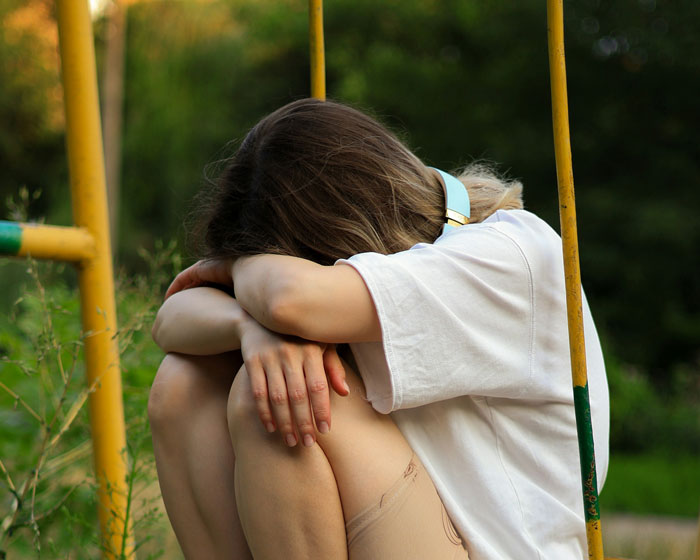 Teen girl sitting alone hugging knees on playground swing, reflecting family conflict over bi daughter lifestyle issues.