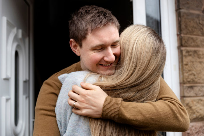 Man hugging woman at doorway, representing family conflict over dad defending bi daughter, causing wife to threaten divorce.