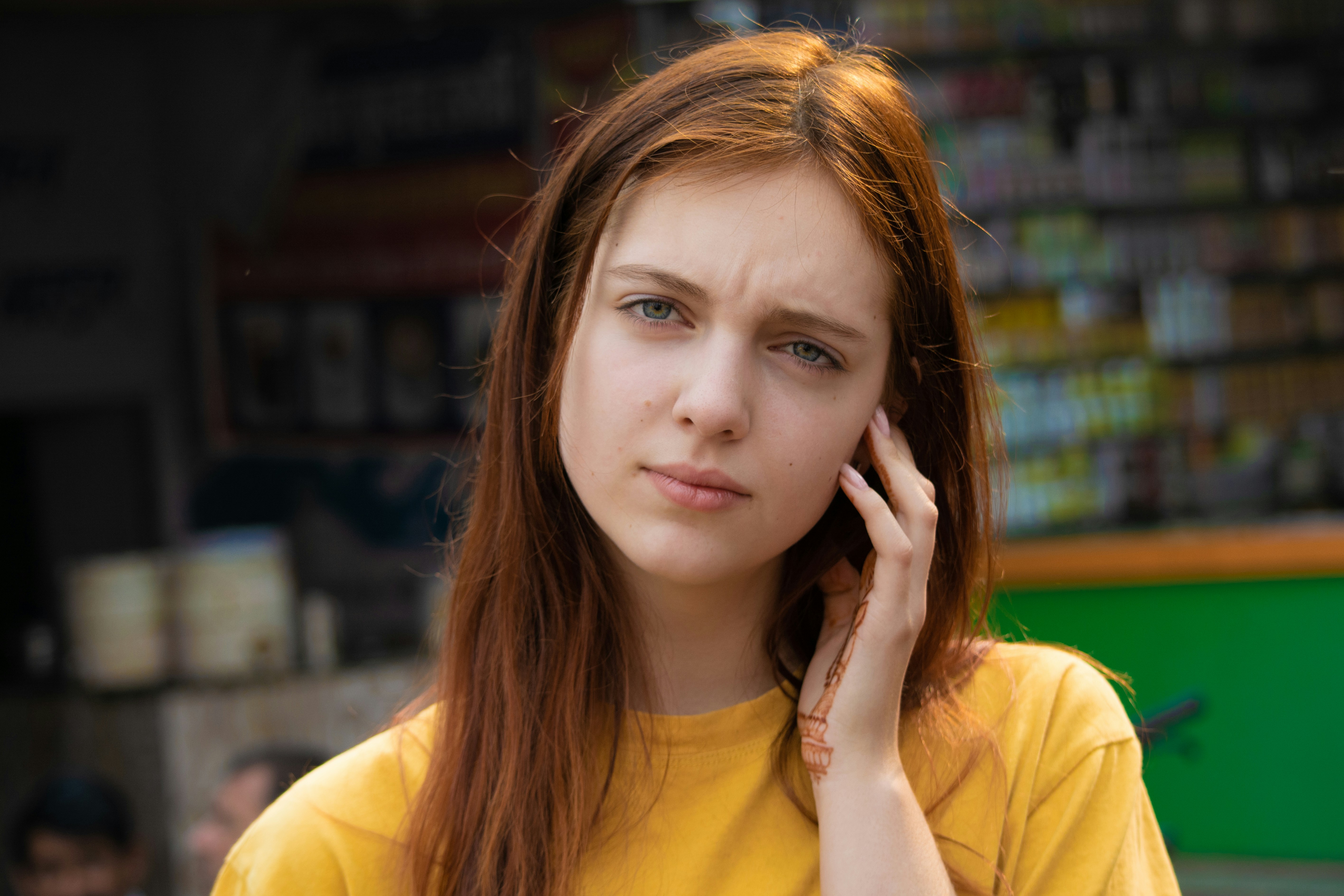 Young woman in a yellow shirt looking thoughtful, touching her face outdoors. Young woman in a yellow shirt looking thoughtful, touching her face outdoors.
