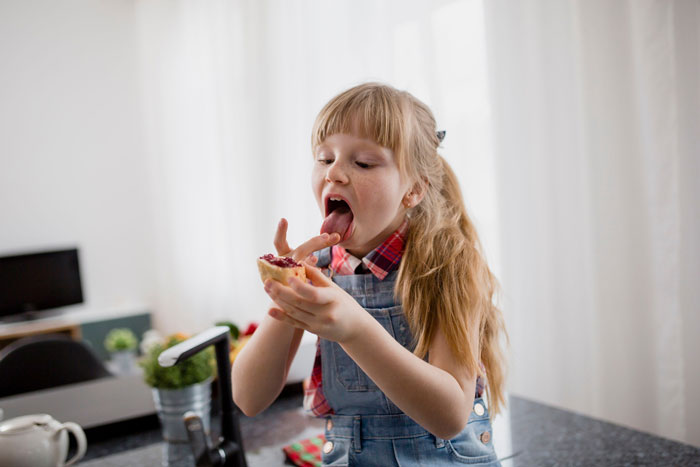 Young girl in a kitchen eating a sandwich, referencing a friend's pantry visits. Young girl in a kitchen eating a sandwich, referencing a friend's pantry visits.