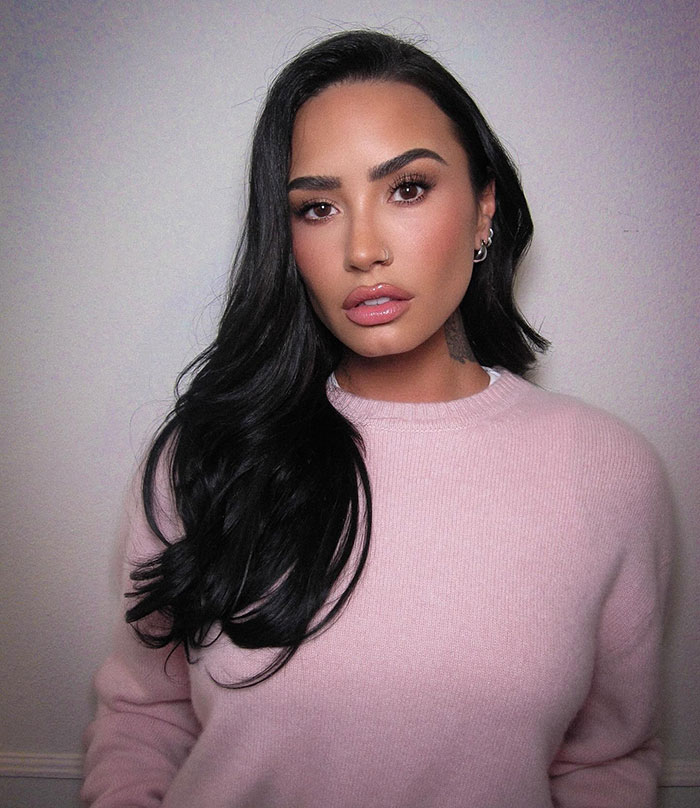 Person in a pink sweater with long dark hair, posing in a neutral setting. Person in a pink sweater with long dark hair, posing in a neutral setting.
