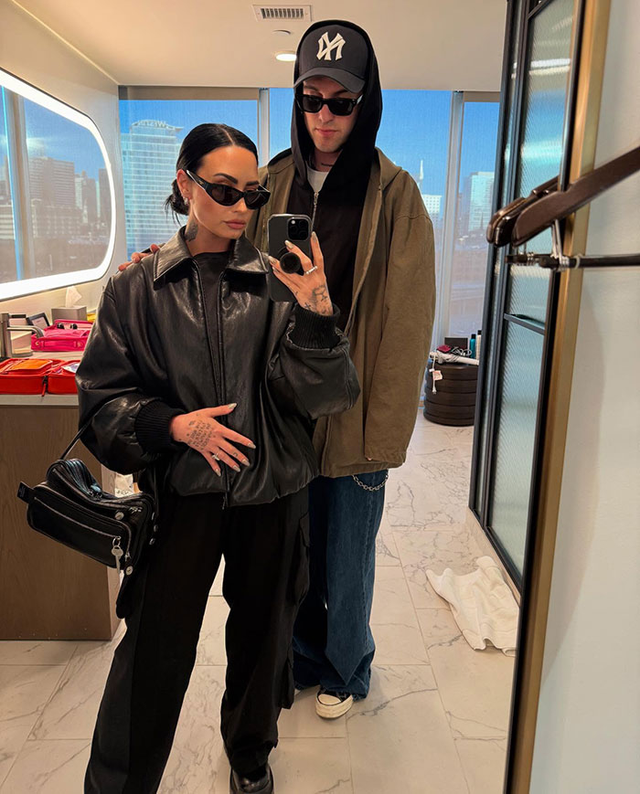 Two people in a modern room, one wearing a leather jacket, another a hat, both with sunglasses, reflecting "skinny" frame. Two people in a modern room, one wearing a leather jacket, another a hat, both with sunglasses, reflecting "skinny" frame.