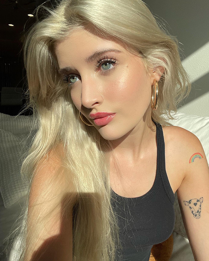 Young woman with long blonde hair, wearing a black tank top, indoors with sunlight on her face, discussing cosmetic surgeries. Young woman with long blonde hair, wearing a black tank top, indoors with sunlight on her face, discussing cosmetic surgeries.