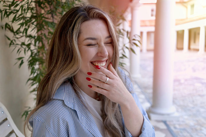 Smiling woman with red nails wearing a ring, enjoying a sunny day near a columned walkway outdoors. Smiling woman with red nails wearing a ring, enjoying a sunny day near a columned walkway outdoors.