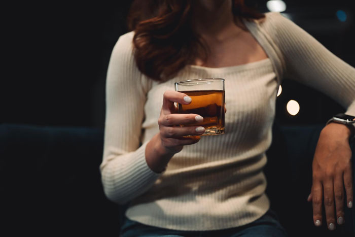 Woman holding a glass of aged scotch, casually seated, unaware of its $500 value. Woman holding a glass of aged scotch, casually seated, unaware of its $500 value.