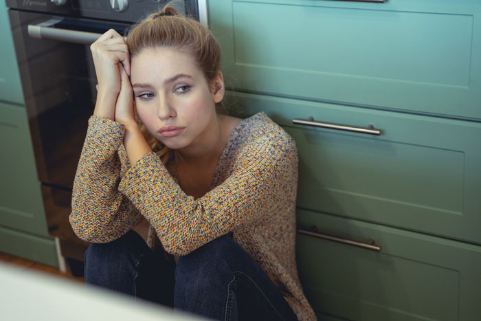 Woman sitting on kitchen floor, looking distressed after drinking aged scotch. Woman sitting on kitchen floor, looking distressed after drinking aged scotch.