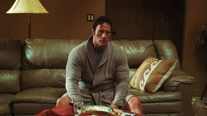 Dwayne Johnson showing impressive transformation in a robe, sitting on a couch preparing for new biopic role. Dwayne Johnson showing impressive transformation in a robe, sitting on a couch preparing for new biopic role.