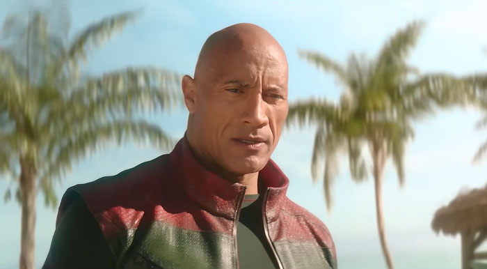 Dwayne Johnson showing impressive transformation in a red and green jacket, standing outdoors with palm trees in the background. Dwayne Johnson showing impressive transformation in a red and green jacket, standing outdoors with palm trees in the background.