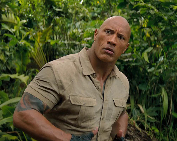 Dwayne Johnson in a jungle setting, wearing a beige shirt, starring in an upcoming movie. Dwayne Johnson in a jungle setting, wearing a beige shirt, starring in an upcoming movie.
