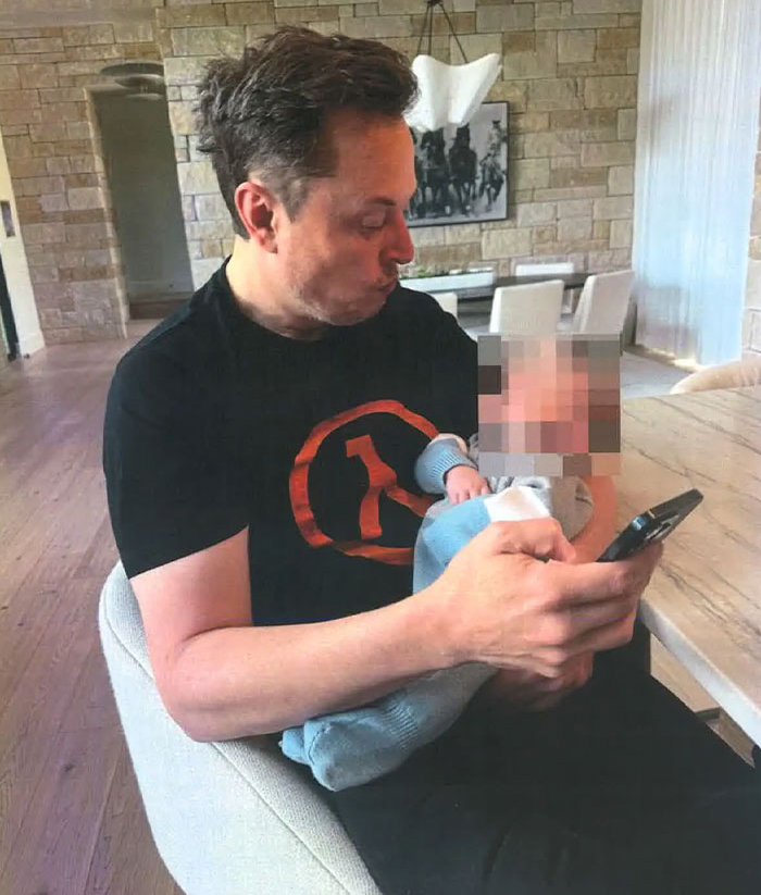 Man sitting in a chair, looking at his phone, holding a baby with a blurred face. Man sitting in a chair, looking at his phone, holding a baby with a blurred face.