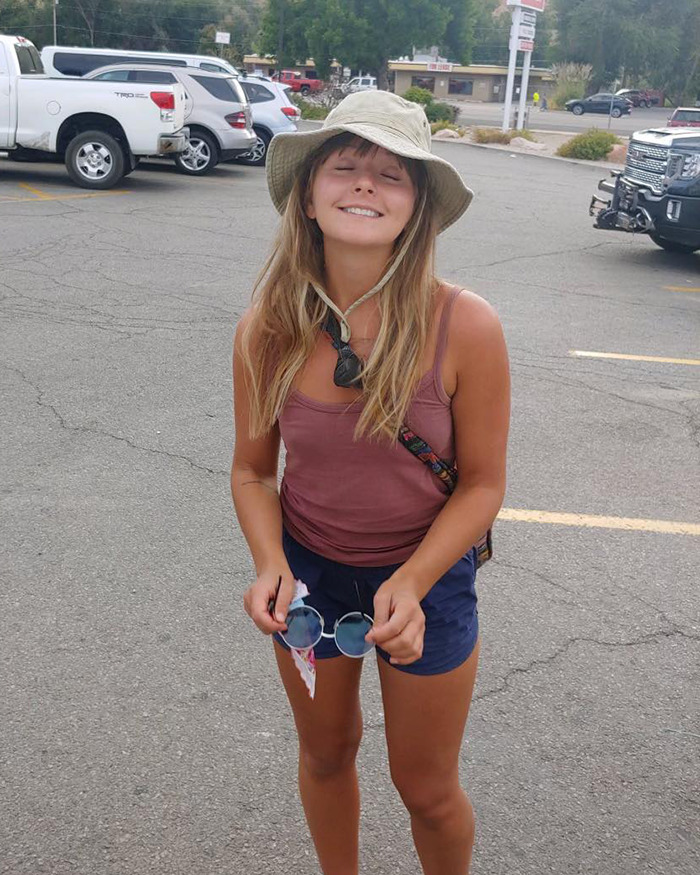 A smiling woman in casual attire and a sun hat, standing in a parking lot. A smiling woman in casual attire and a sun hat, standing in a parking lot.
