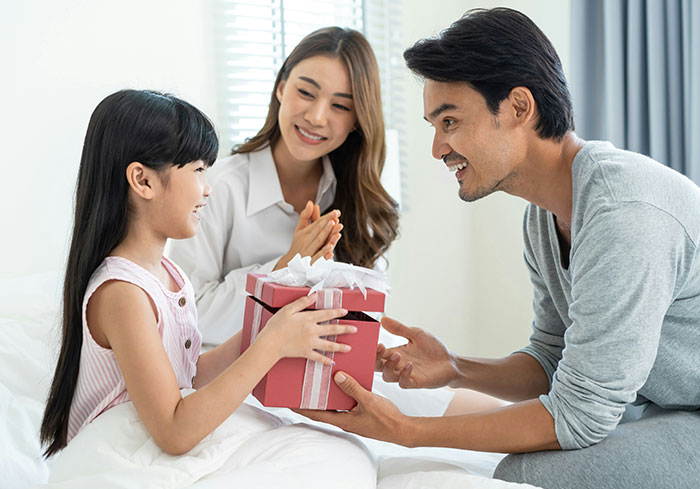A family shares a gift, sitting together on a bed, smiling and enjoying a moment. A family shares a gift, sitting together on a bed, smiling and enjoying a moment.