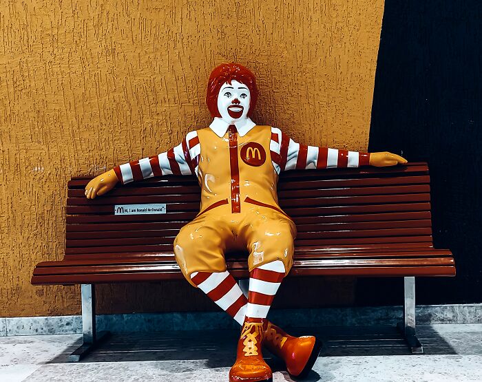 Statue of Ronald McDonald sitting on a bench, representing skillful branding and marketing in public spaces.
