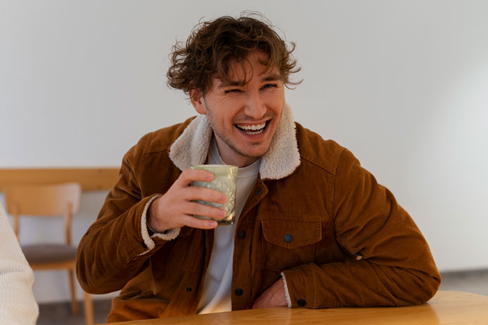 Man laughing with a drink at a table, feeling cheerful despite being dumped before Valentine's. Man laughing with a drink at a table, feeling cheerful despite being dumped before Valentine's.