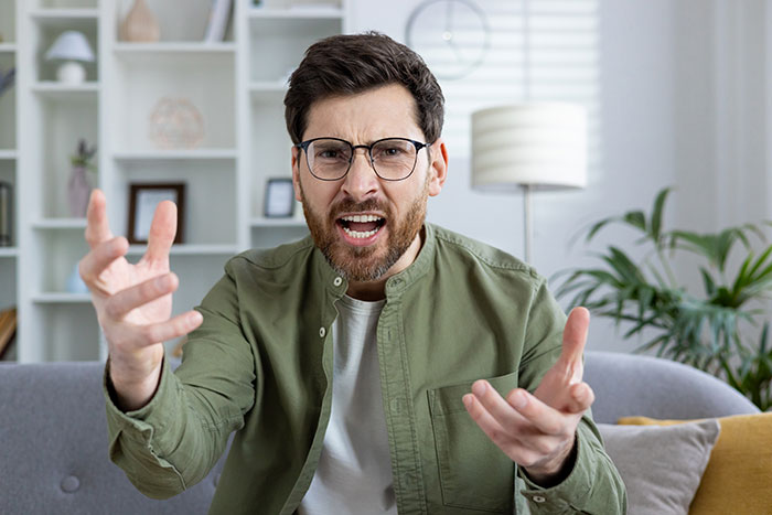 Man in green jacket and glasses looking upset, gesturing with hands, in a bright room with plants and shelves. Man in green jacket and glasses looking upset, gesturing with hands, in a bright room with plants and shelves.